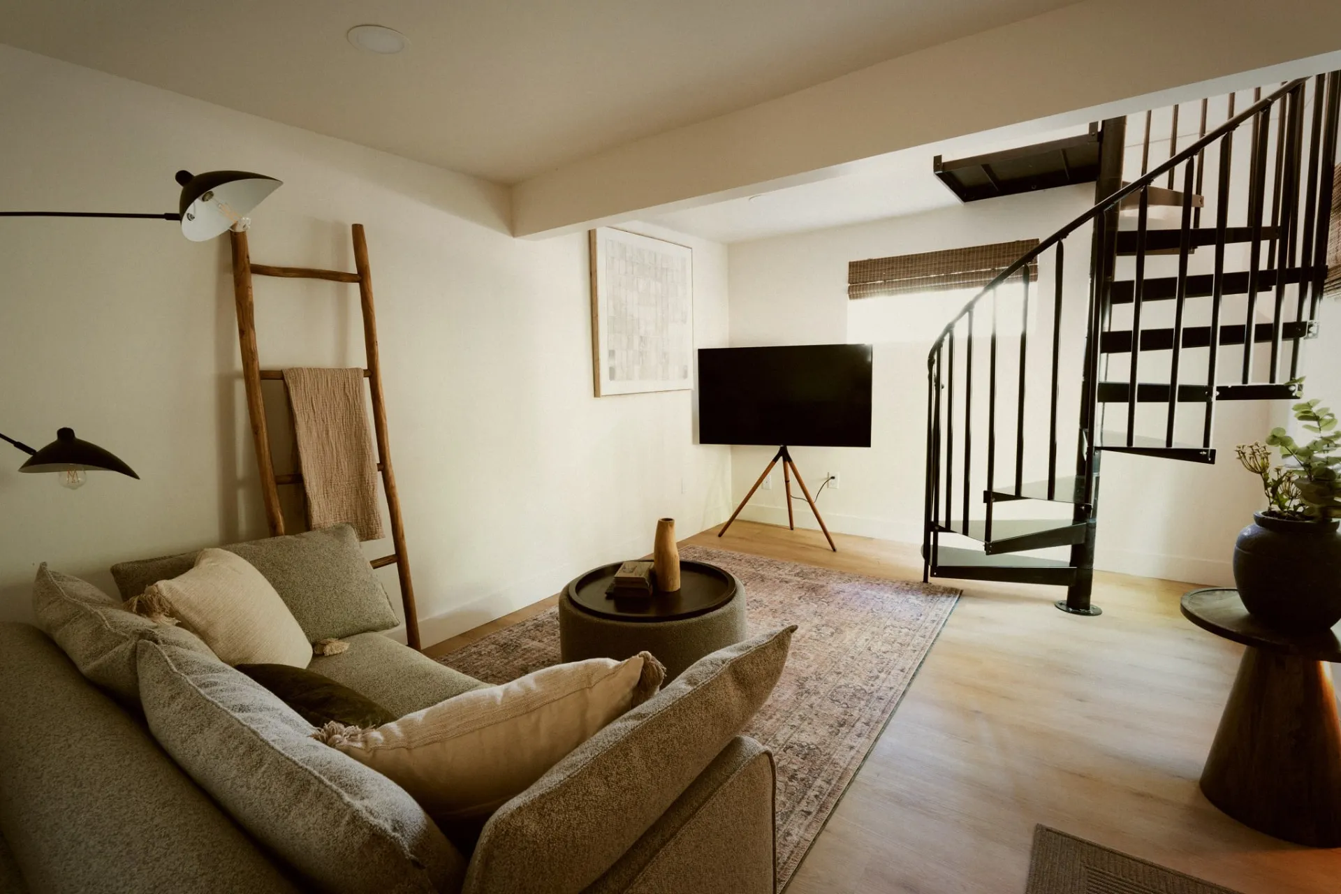 The downstairs den, with a sofa, television and black spiral staircase